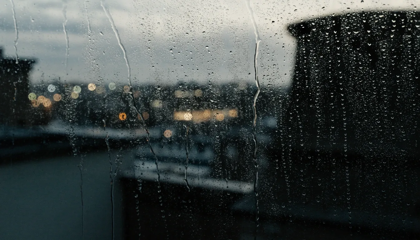 Rain-streaked window looking out over a dim London rooftop at dusk