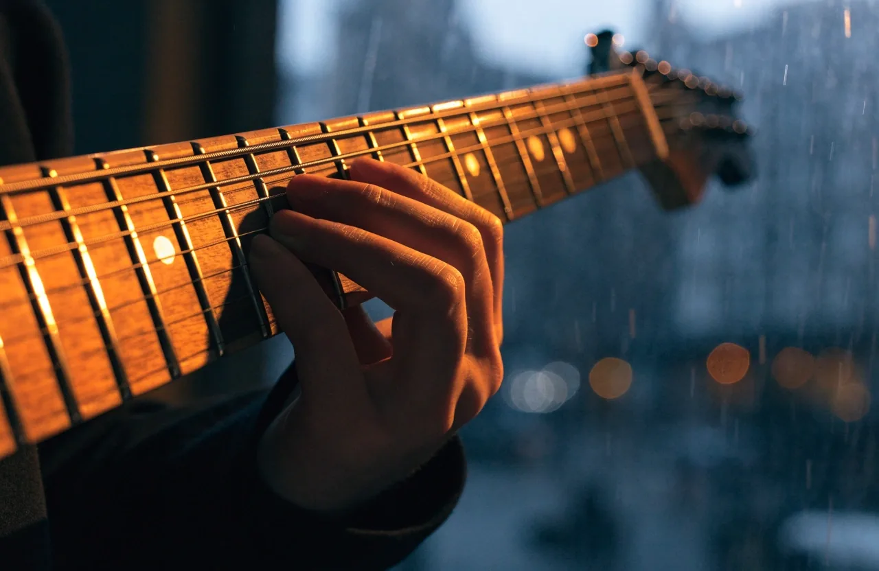 Close crop of a student's hand on a guitar fretboard catching amber light